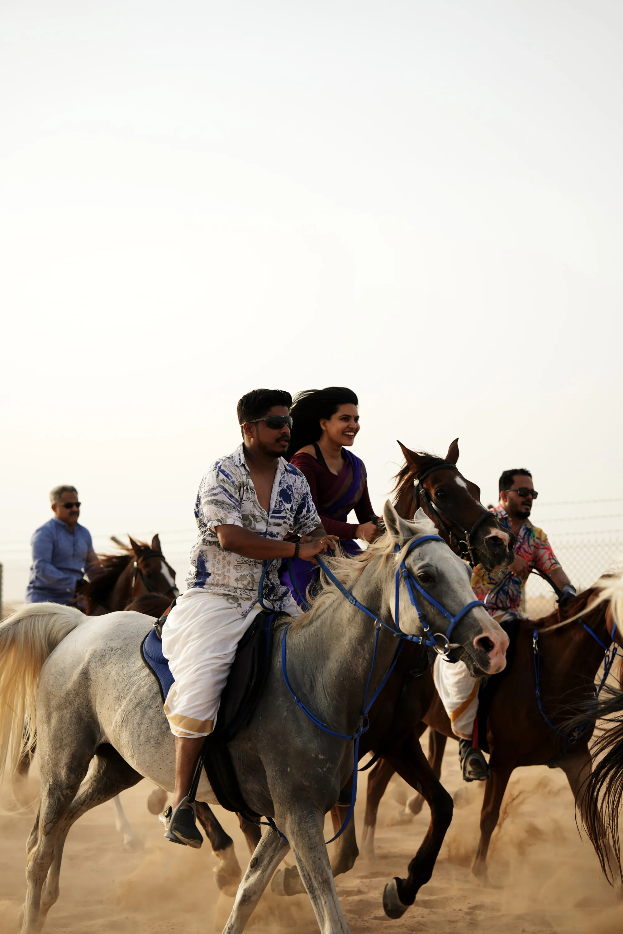 A man and a woman riding a grey horse together at a canter, other riders close behind