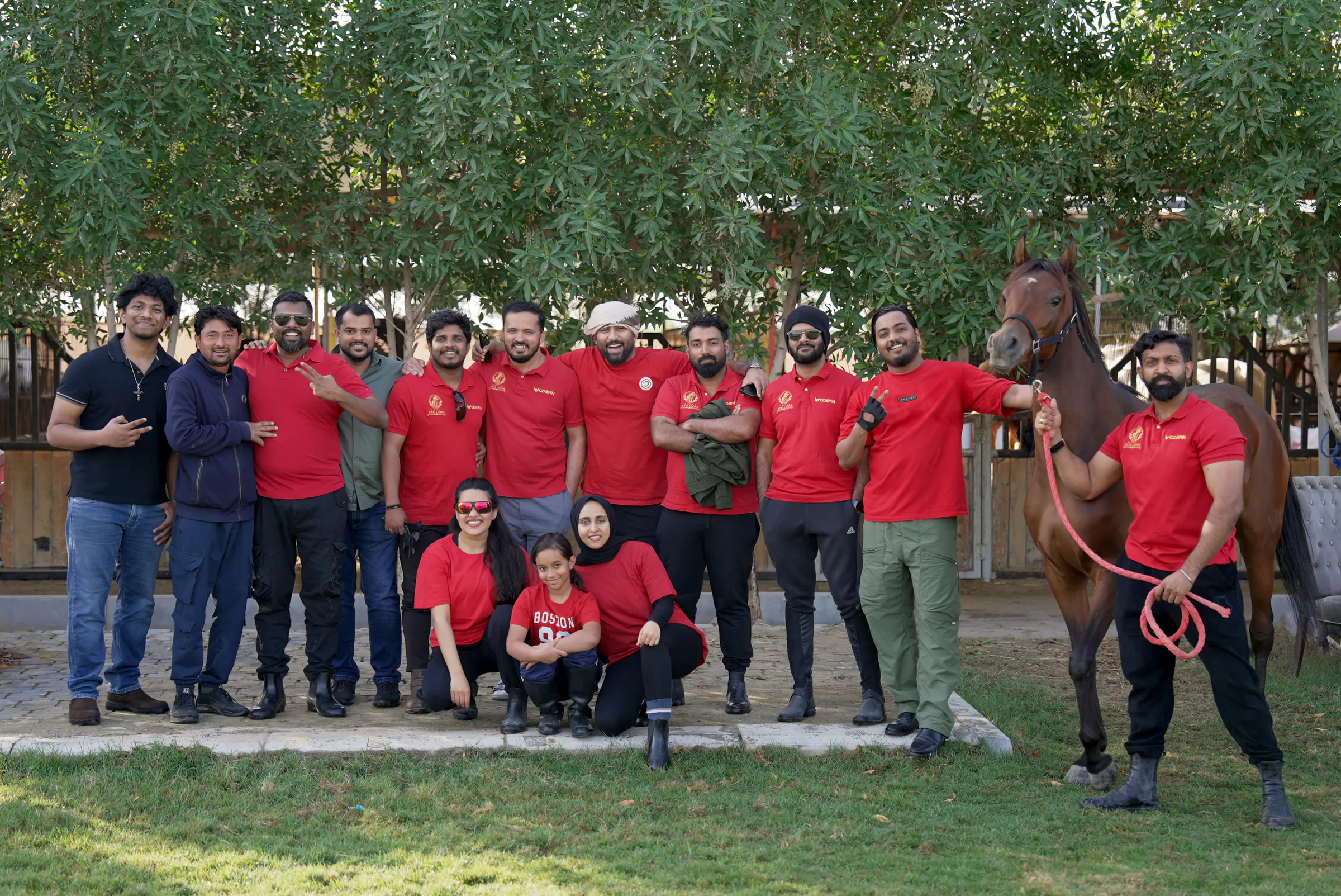 Royal Stallions members in red club shirts with a bay horse at the stables