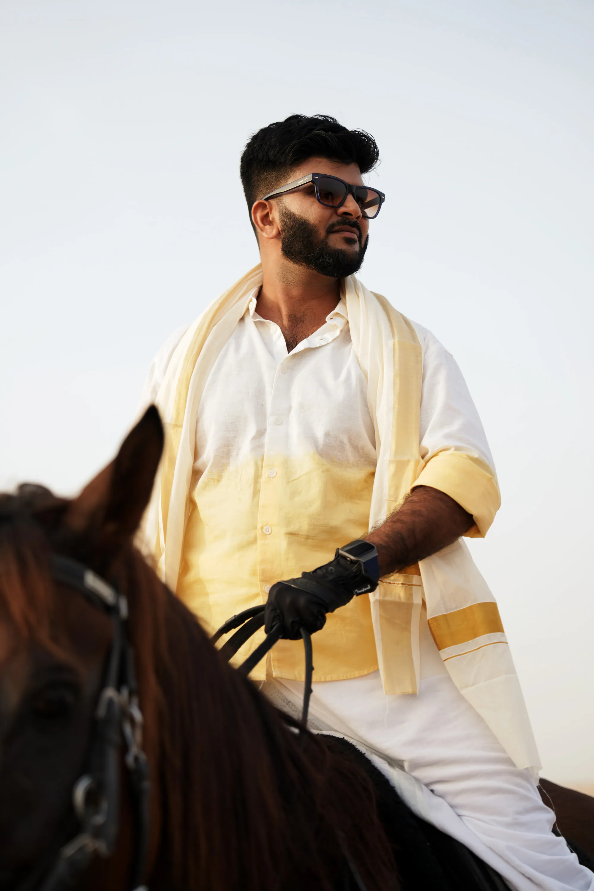 A rider in a cream and gold Kerala shawl on a dark horse